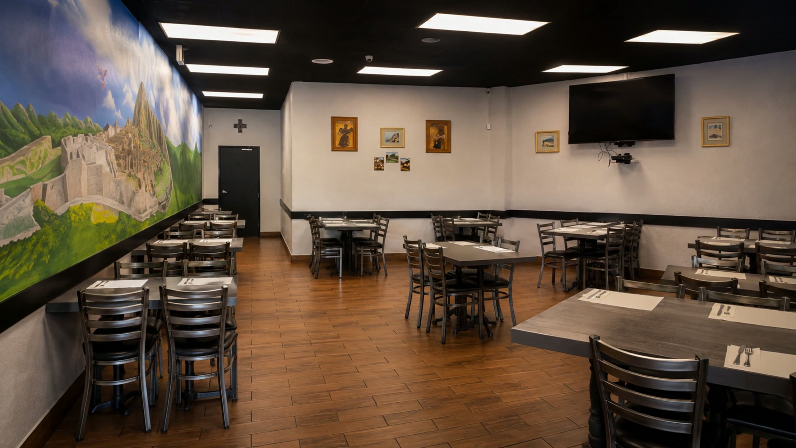 Inti's dining room: a painted mural of Machu Picchu along the left wall, dark tables with silver chairs, framed art and a black ceiling.