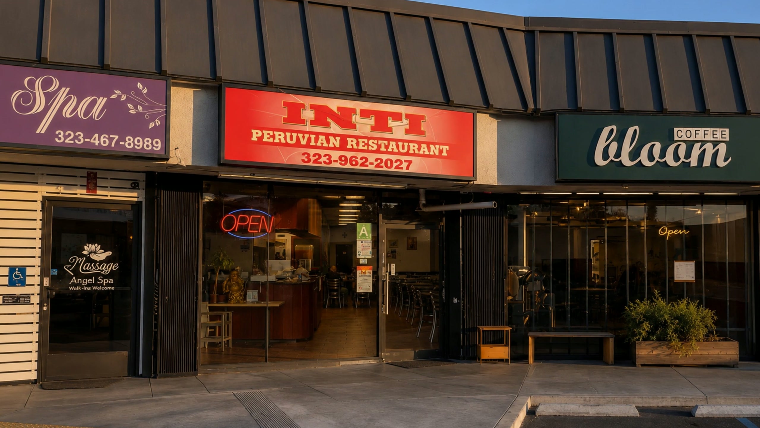 Inti's storefront at golden hour: the red Inti Peruvian Restaurant sign above reflective glass doors, between Angel Spa and Bloom Coffee.